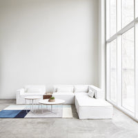 White sectional sofa with a light grey floor and patterned blue and cream rug, enhancing a modern minimalist aesthetic.