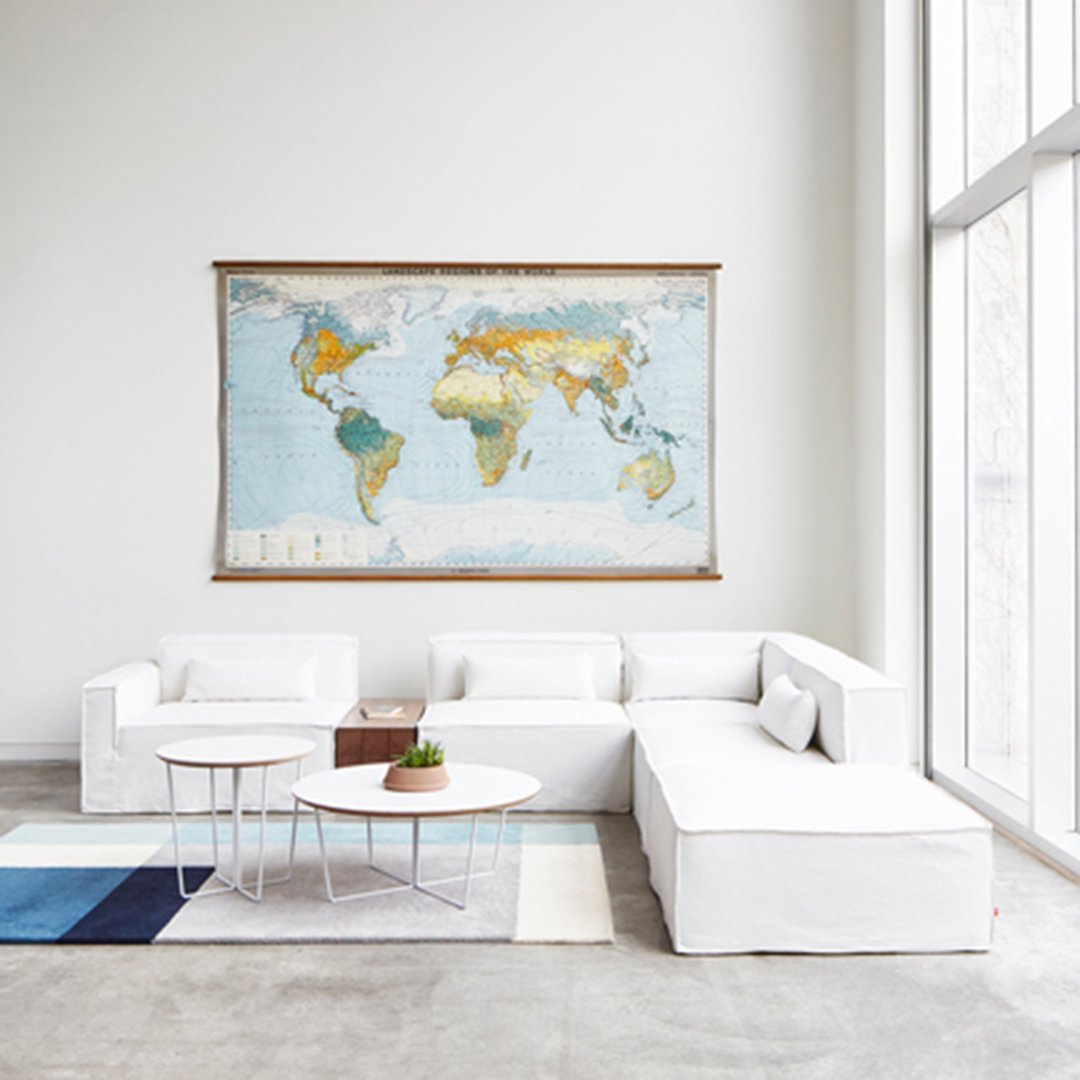 Vintage world map in soft blues, earthy yellows, and greens, complementing a modern, minimalist white interior.