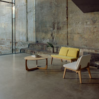 Modern living room with a yellow and white sofa, accented by light wood furniture against a textured concrete wall.