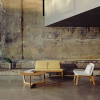 Mid-century modern furniture featuring a mustard yellow sofa and white chair against a textured concrete backdrop.
