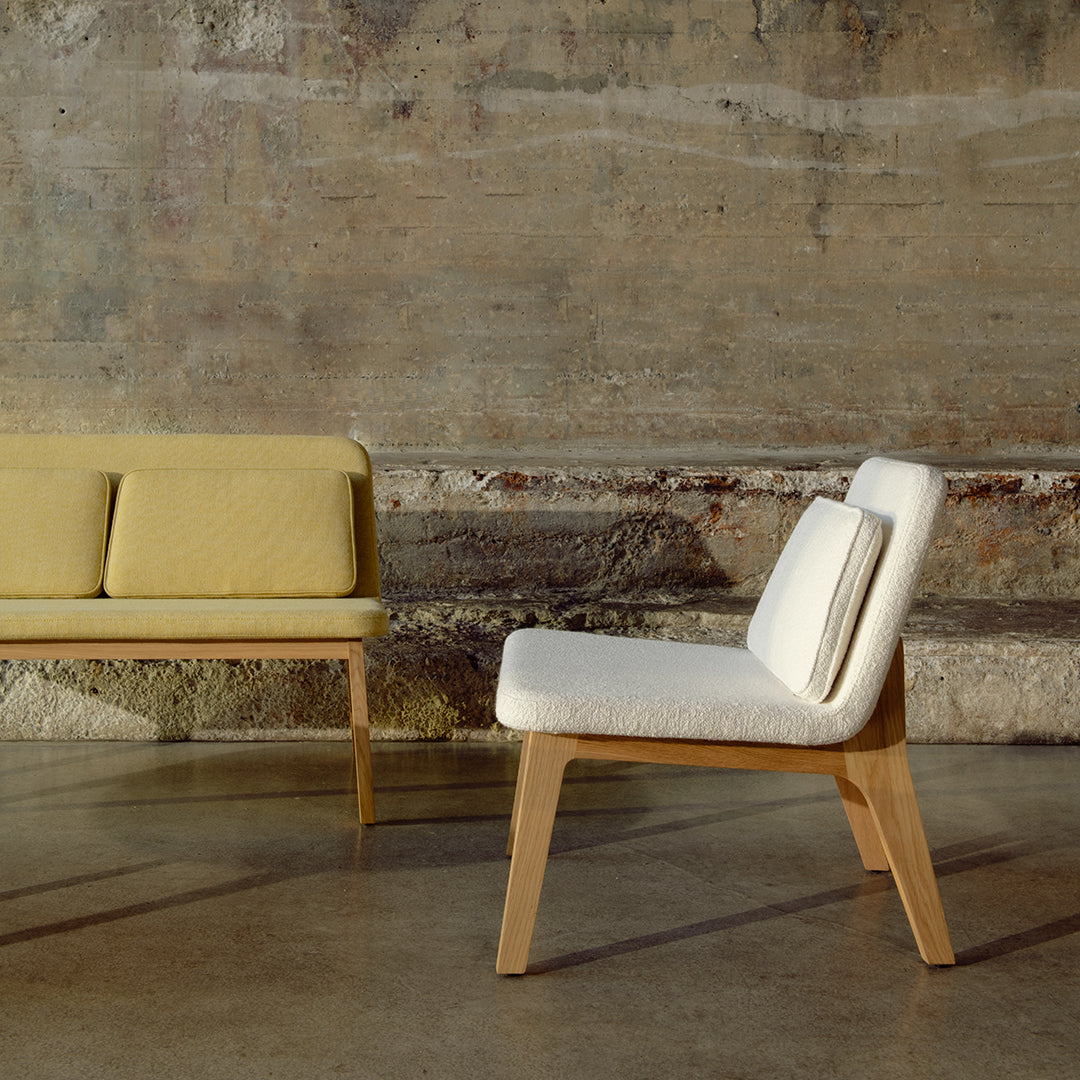 Two modern chairs featuring soft yellow and white upholstery against a rustic concrete backdrop.