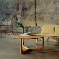 Modern round wooden coffee table with a light natural finish, paired with a soft yellow sofa against a textured background.