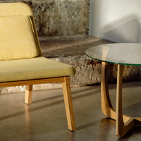 Yellow upholstered chair with wooden legs next to a minimalist glass-top table, set on a textured stone background.