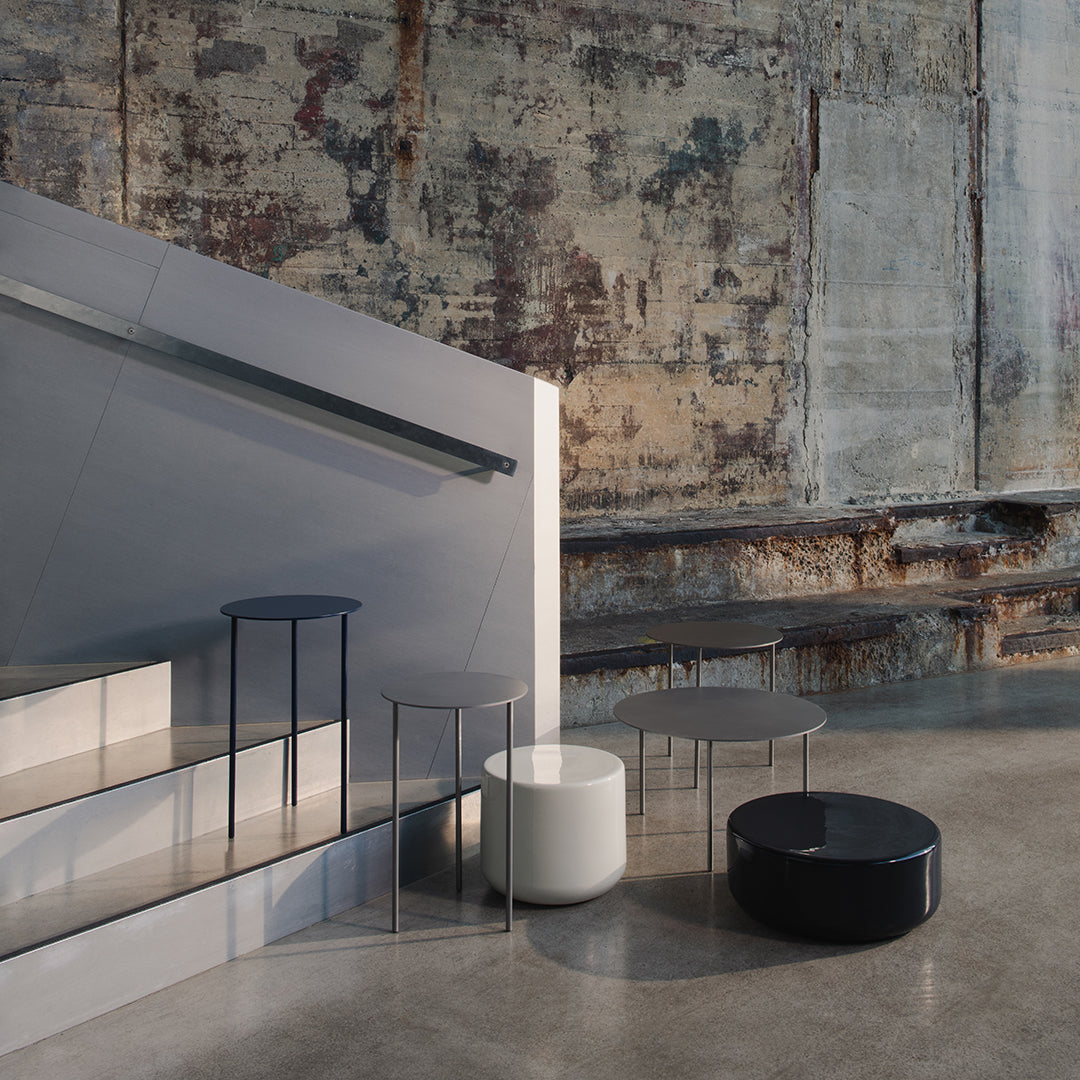 Modern minimalist tables in white, black, and gray, featuring sleek lines and reflective surfaces.