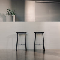 "Two black bar stools against a light gray wall with sleek, modern design and minimalistic aesthetic."