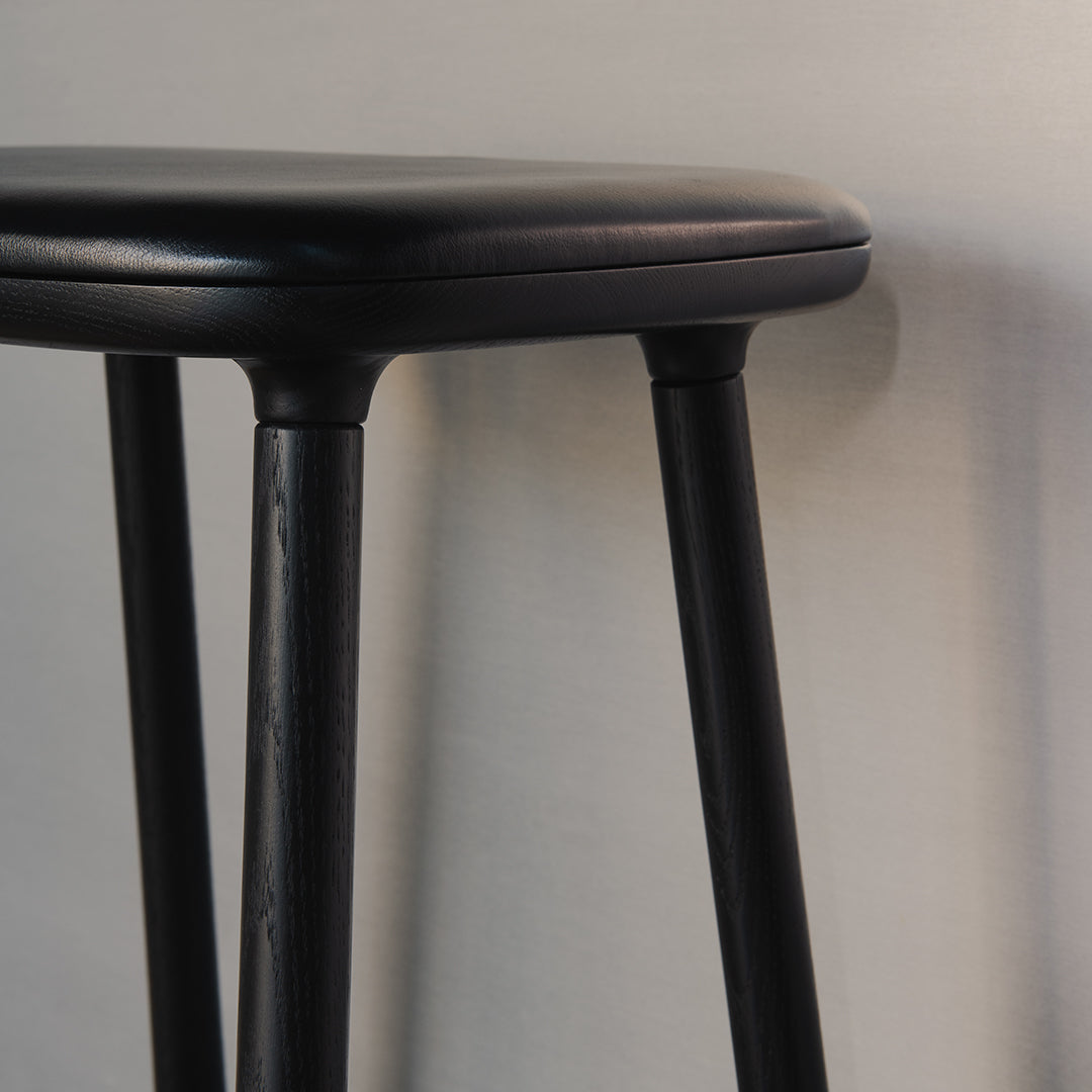 Black round bar stool with smooth, sleek finish and sturdy black legs against a light gray background.