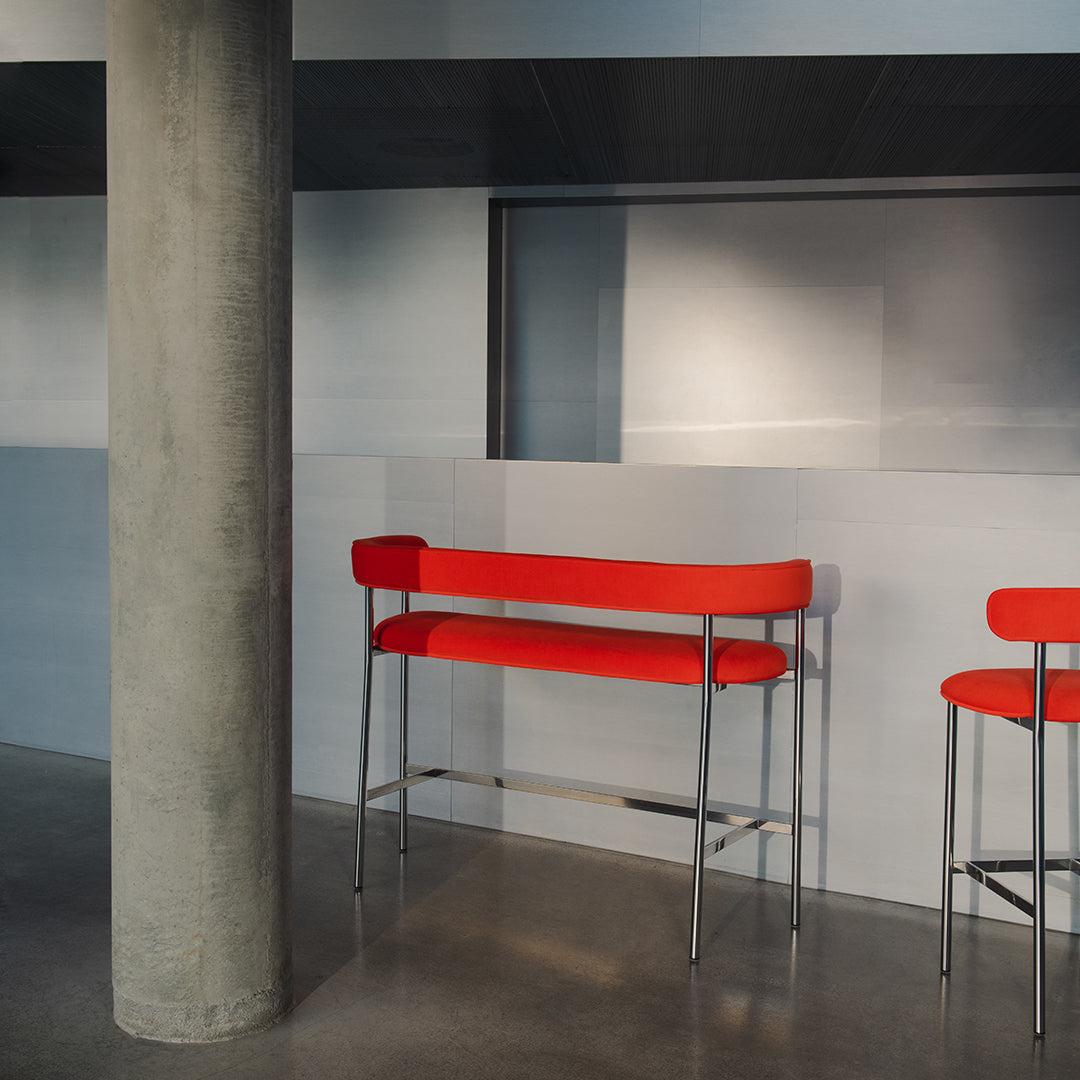 Red bar stools with minimalist design against a sleek gray backdrop and concrete pillar. Modern color contrast.