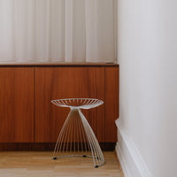 Stylish white wire stool with sleek lines against a warm wood background, perfect for modern decor.