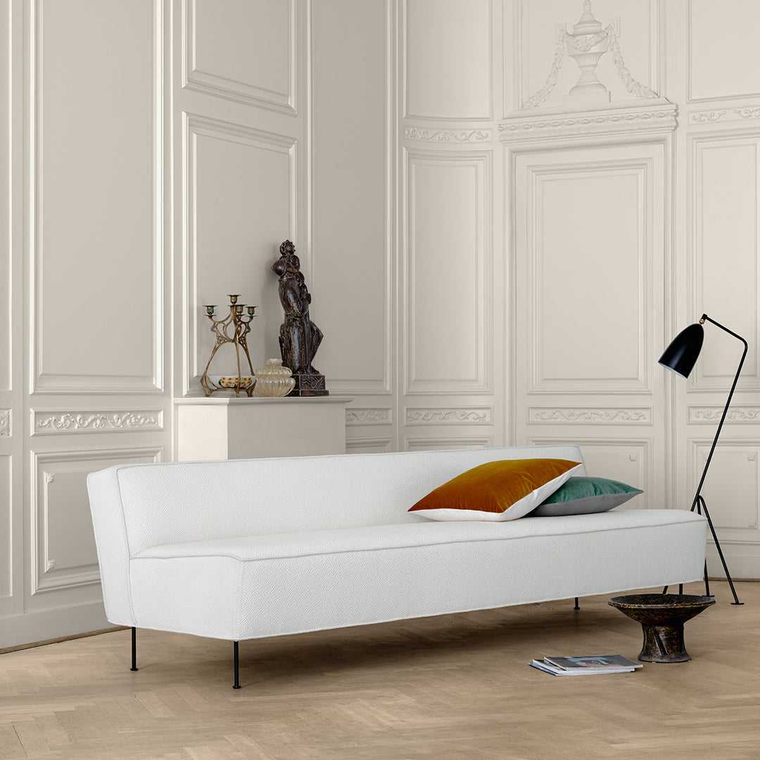 Sleek white sofa with colorful pillows in shades of green and rust against a classic backdrop. Modern minimalist design.