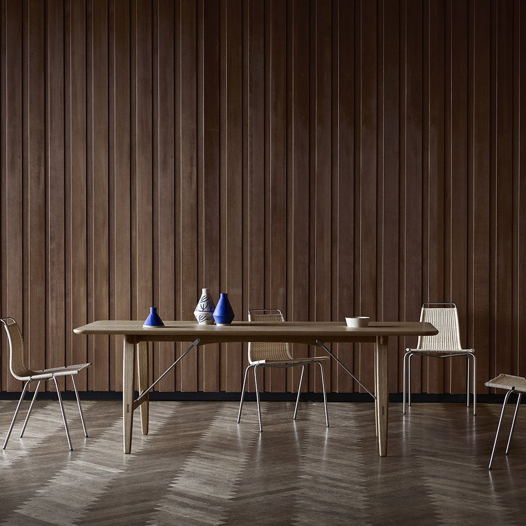 Natural wood dining table with light brown finish, complemented by blue and white decorative vases against a dark wooden wall.