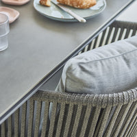 Gray cushion on a textured woven chair beside a minimalist gray table and pastel-colored plates.