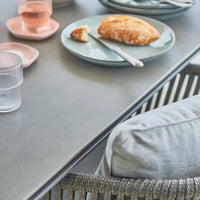 "Soft grey table with textured patterns, light blue dish, pink plates, and clear glassware, creating a cozy dining scene."