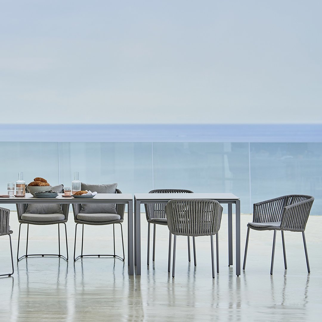 Elegant gray outdoor dining set with woven chairs, set against a serene ocean view backdrop. Perfect for alfresco dining.