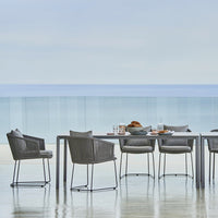 "Elegant outdoor dining set with grey woven chairs and sleek table against a serene blue ocean backdrop."