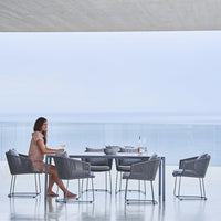 Gray outdoor dining set with sleek modern lines, featuring woven chairs on a serene, light-colored patio.
