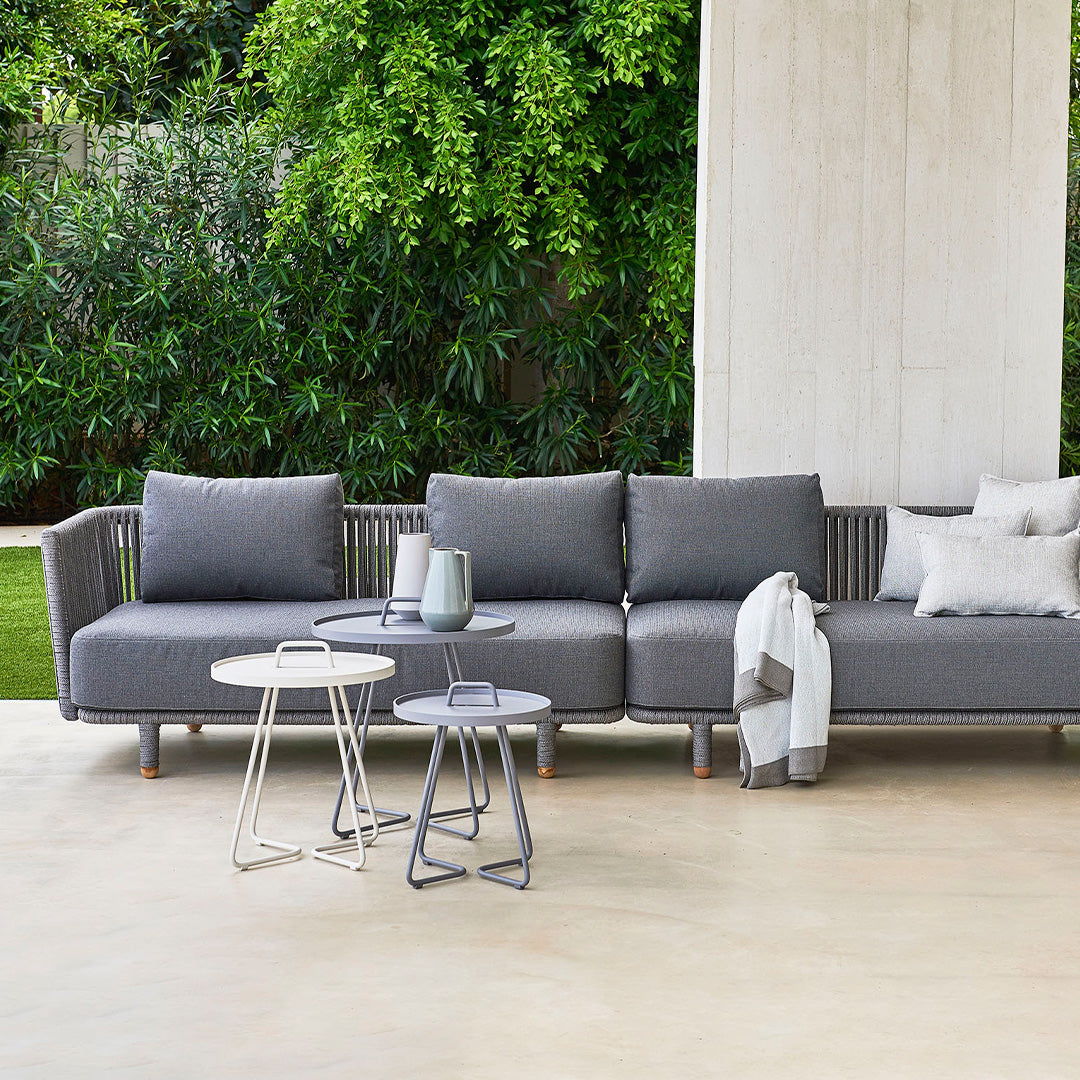 Gray outdoor sectional sofa with textured fabric, paired with sleek white and silver side tables in a natural setting.