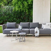 Gray outdoor sectional sofa with textured fabric, paired with sleek white and silver side tables in a natural setting.