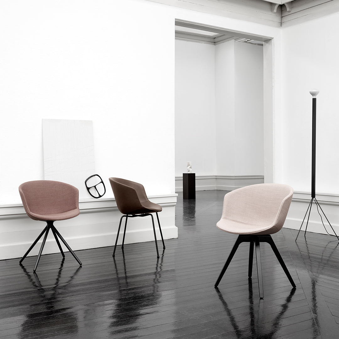 Modern chairs in soft pink, brown, and neutral tones with sleek black legs against a minimalist backdrop.