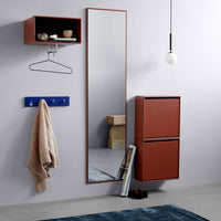 Red wall-mounted storage, blue hanging rack, beige knitted sweater, and a gray textured rug. Modern minimalist design aesthetics.
