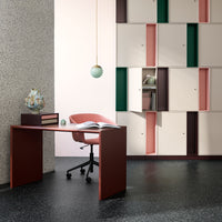 Modern workspace featuring a pink chair, burgundy desk, and multi-colored storage units in green, pink, and cream.