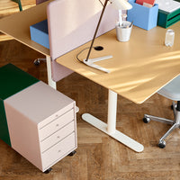 Stylish workspace featuring a tan desk, pastel pink file cabinet, green accents, and blue organizational boxes.