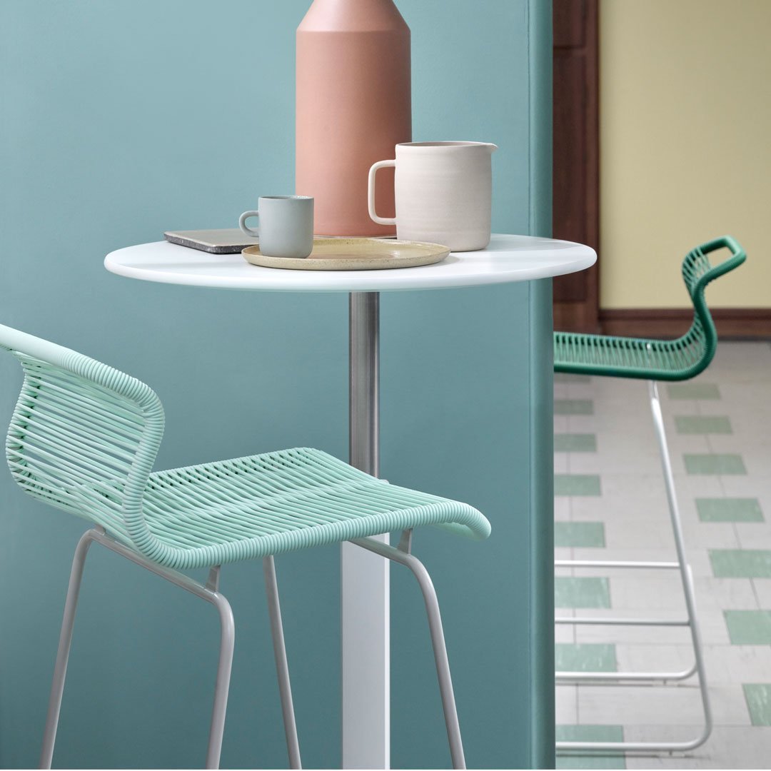 Aqua chairs and soft pastel-hued tableware create a fresh, modern dining scene with geometric floor patterns.