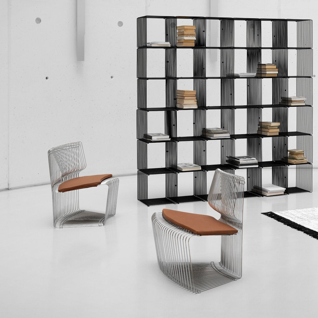 Modern wire chairs with transparent patterns and warm brown cushions, set against a sleek black shelving unit.