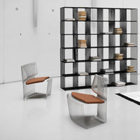 Modern wire chairs with transparent patterns and warm brown cushions, set against a sleek black shelving unit.