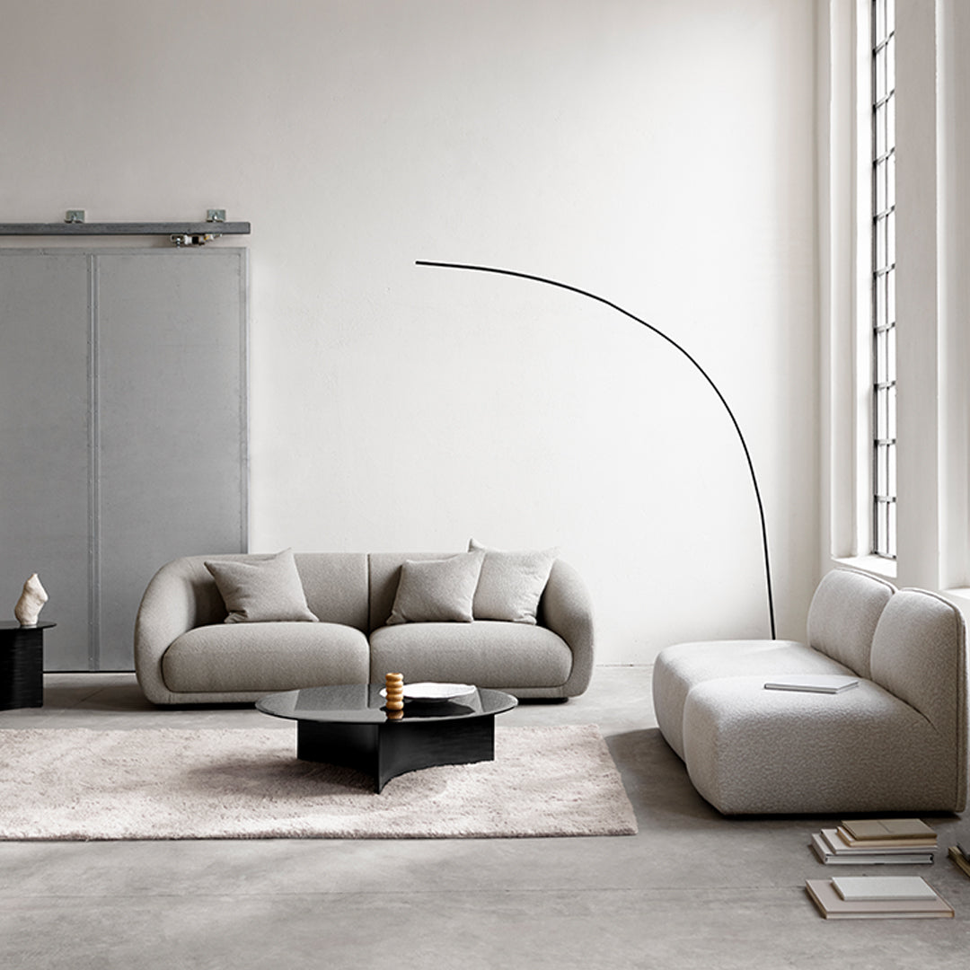 Gray curved sofas with soft cushions and a geometric black coffee table on a light beige rug in a minimalist setting.