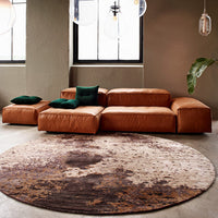 Brown leather sofa with green pillows and a circular rug featuring earthy tones and abstract patterns.