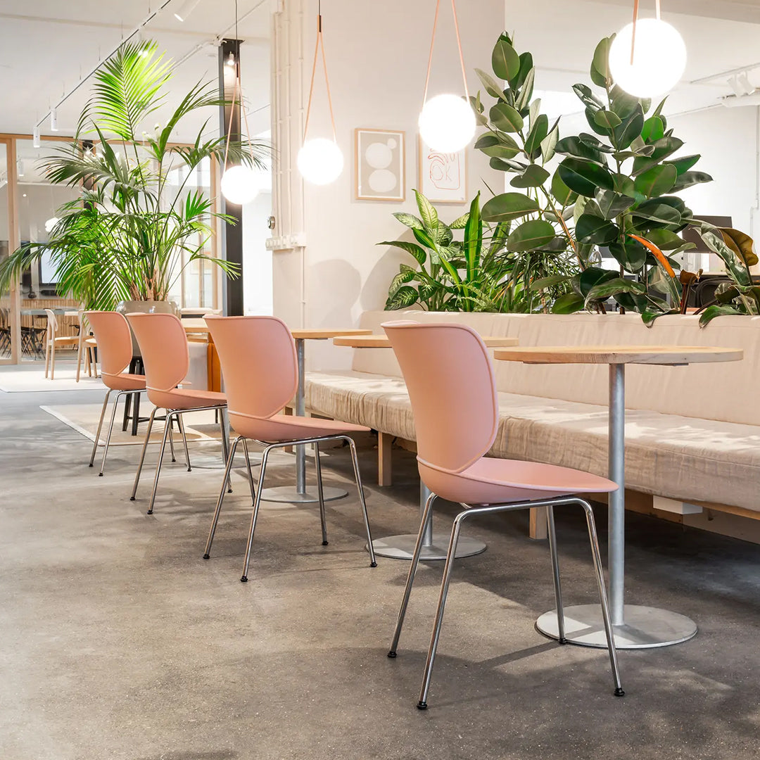 Soft pink chairs with sleek silver legs against a backdrop of green plants in a modern, bright setting.