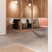 Modern workspace with light pink and white chairs, wooden accents, and a concrete floor, creating a minimalist aesthetic.
