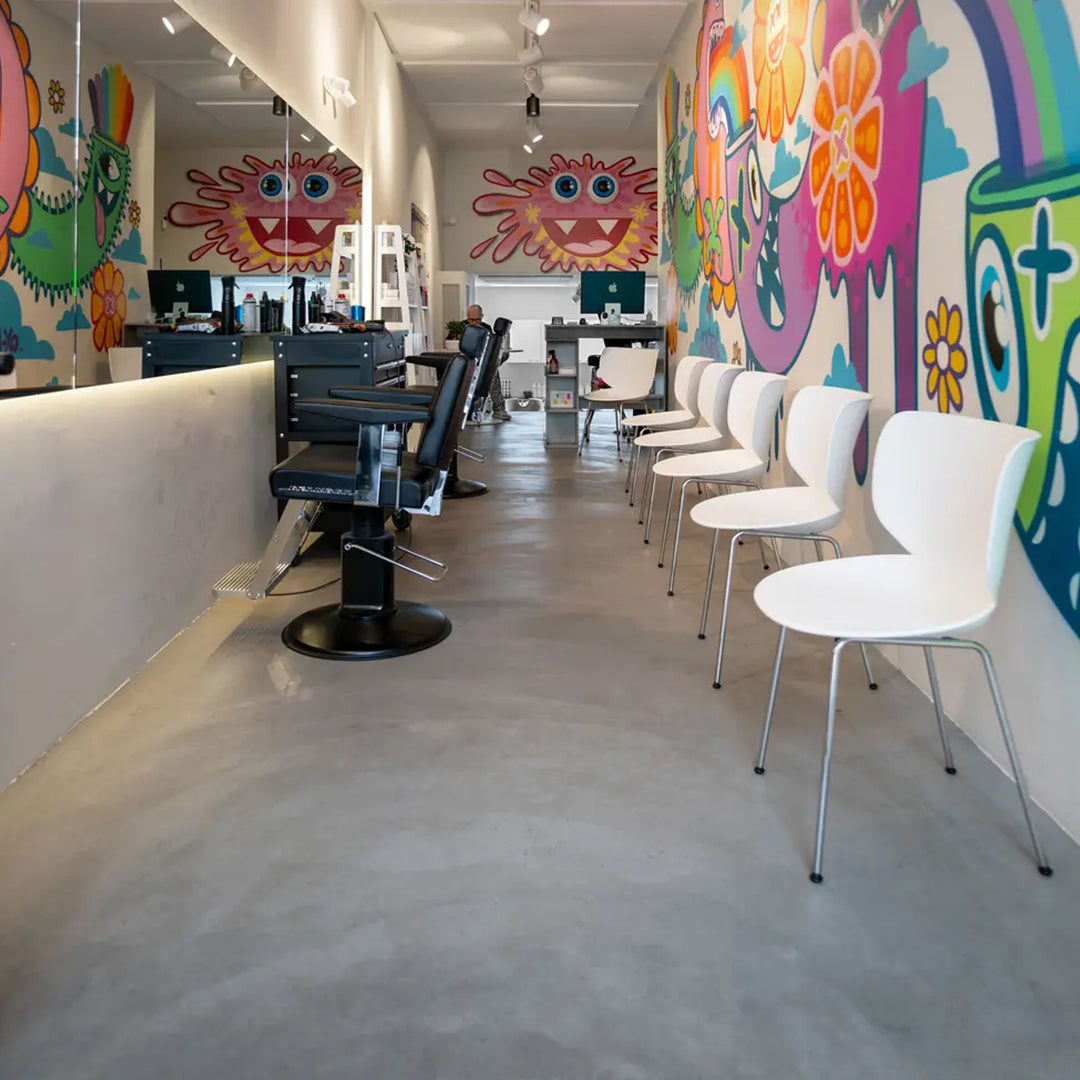 Bright and colorful salon interior featuring vibrant wall art, modern white chairs, and a sleek concrete floor.