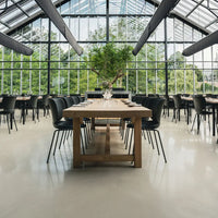 Modern black chairs with a wooden table, surrounded by lush greenery and large glass windows in a bright, airy setting.