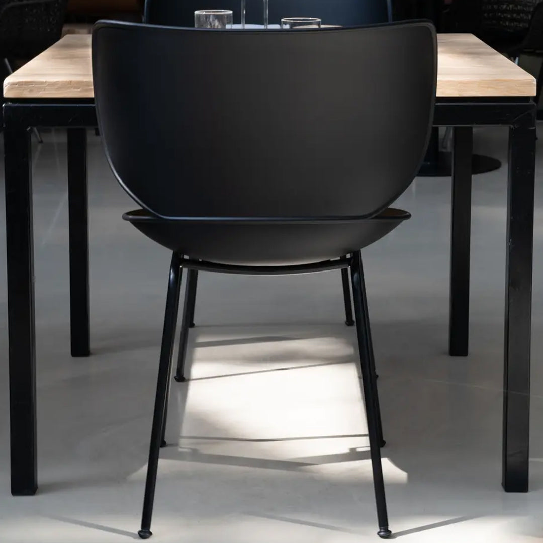 Black minimalist chair against a light wooden table, showcasing sleek lines and a modern design.