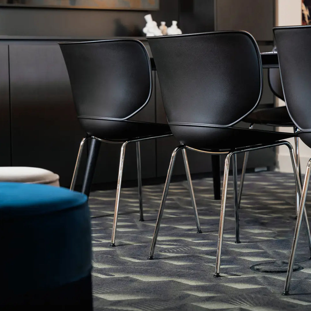 Sleek black dining chairs on a textured dark gray patterned carpet with a vibrant blue ottoman accent.