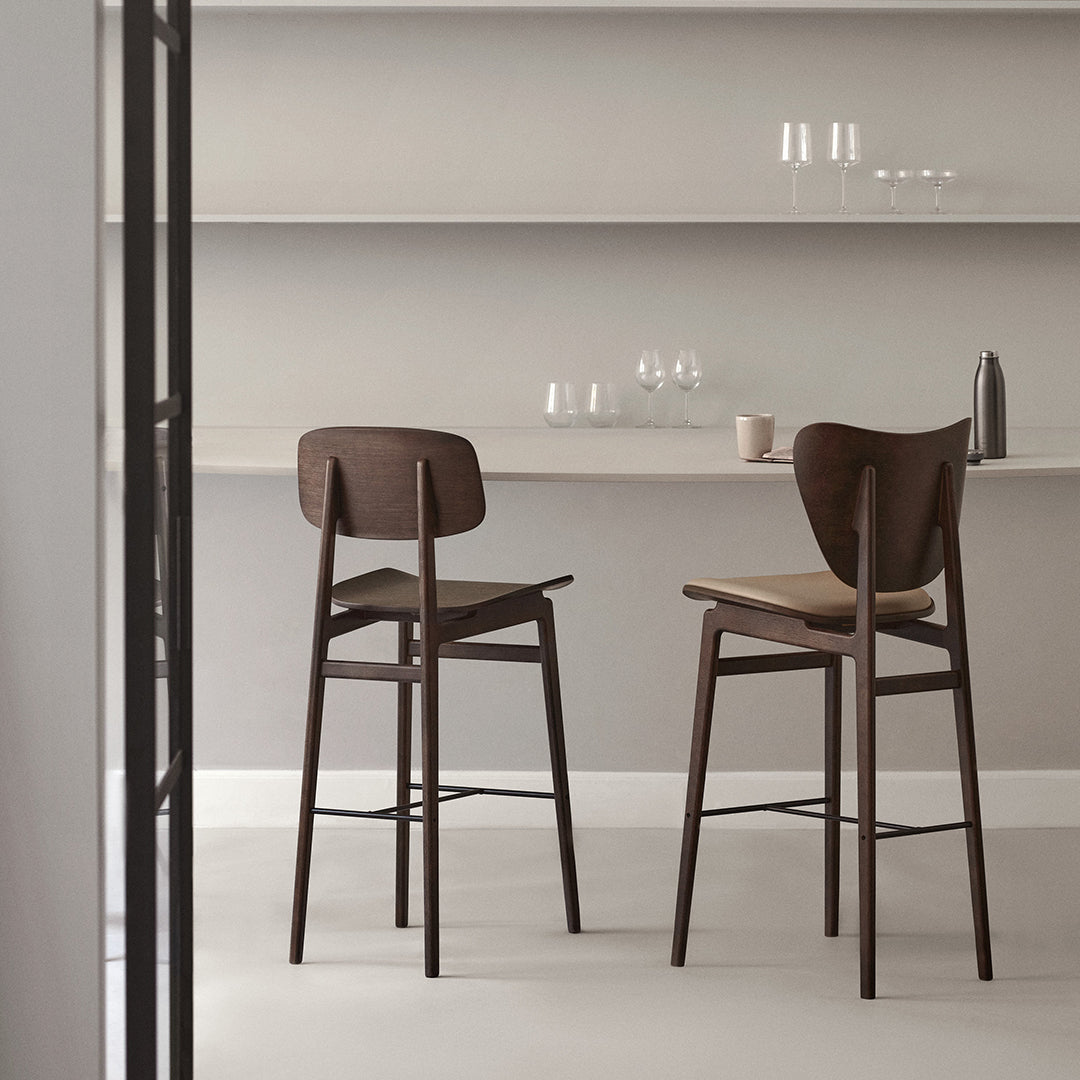 Two modern wooden bar stools in rich brown tones, featuring a minimalistic design and textured seat pattern.
