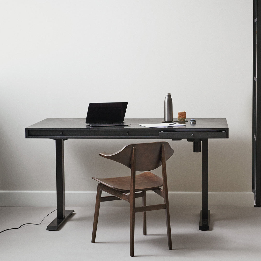 Minimalist black desk with a sleek design, paired with a warm wood chair against a neutral wall.