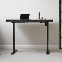 Black standing desk with a sleek matte finish and minimalistic design, set against a light gray wall.