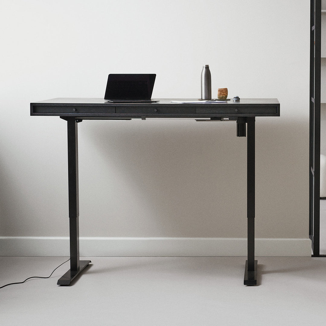 Modern black standing desk with a sleek surface and minimalist design, set against a light neutral background.
