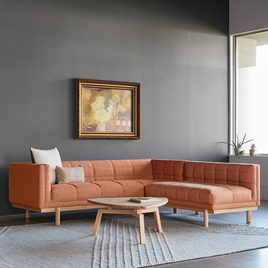 "Orange sectional sofa with tufted fabric, light wood legs, and minimalist decor on a gray backdrop."
