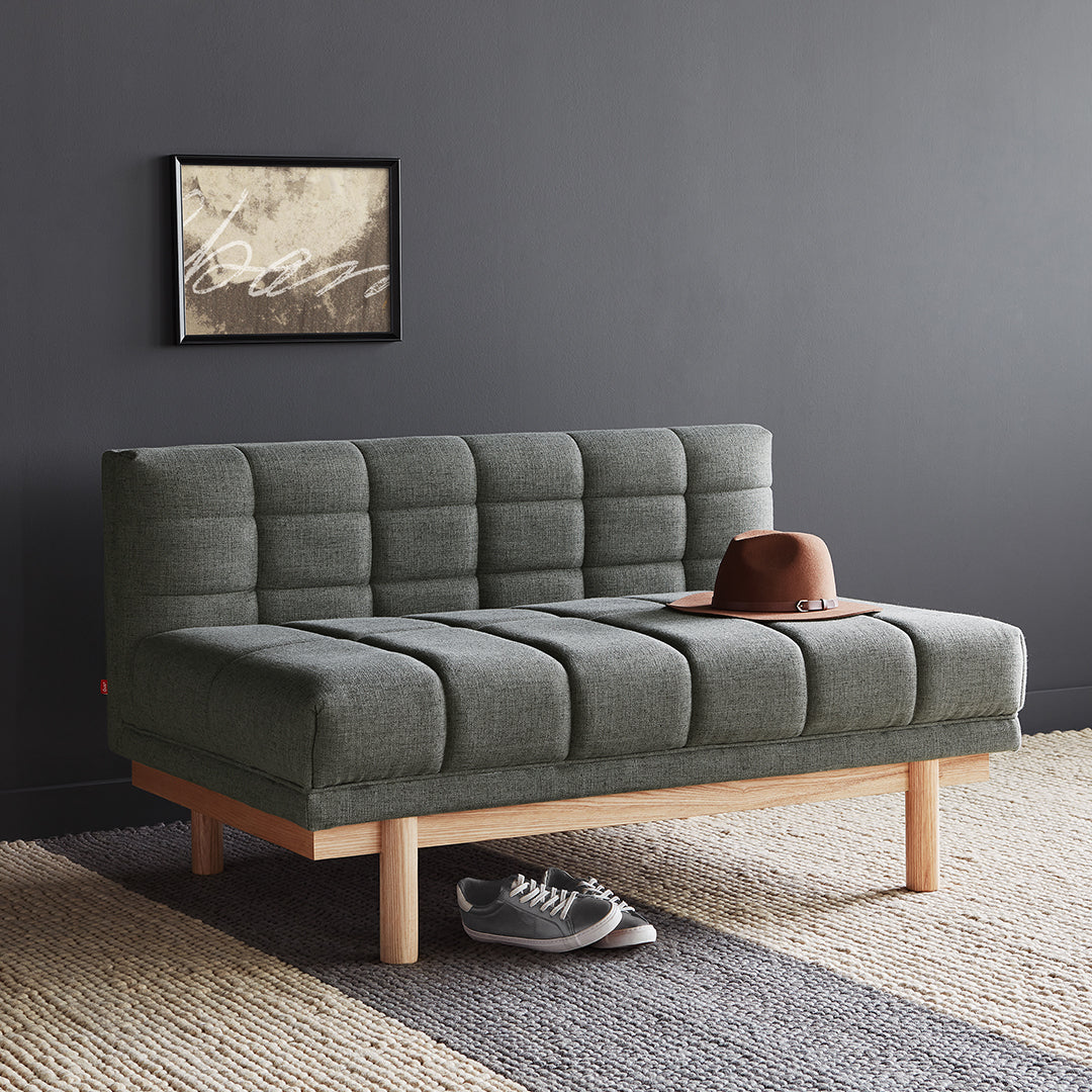 Gray tufted fabric sofa with wooden legs, complemented by earthy tones in rug and dark wall backdrop.
