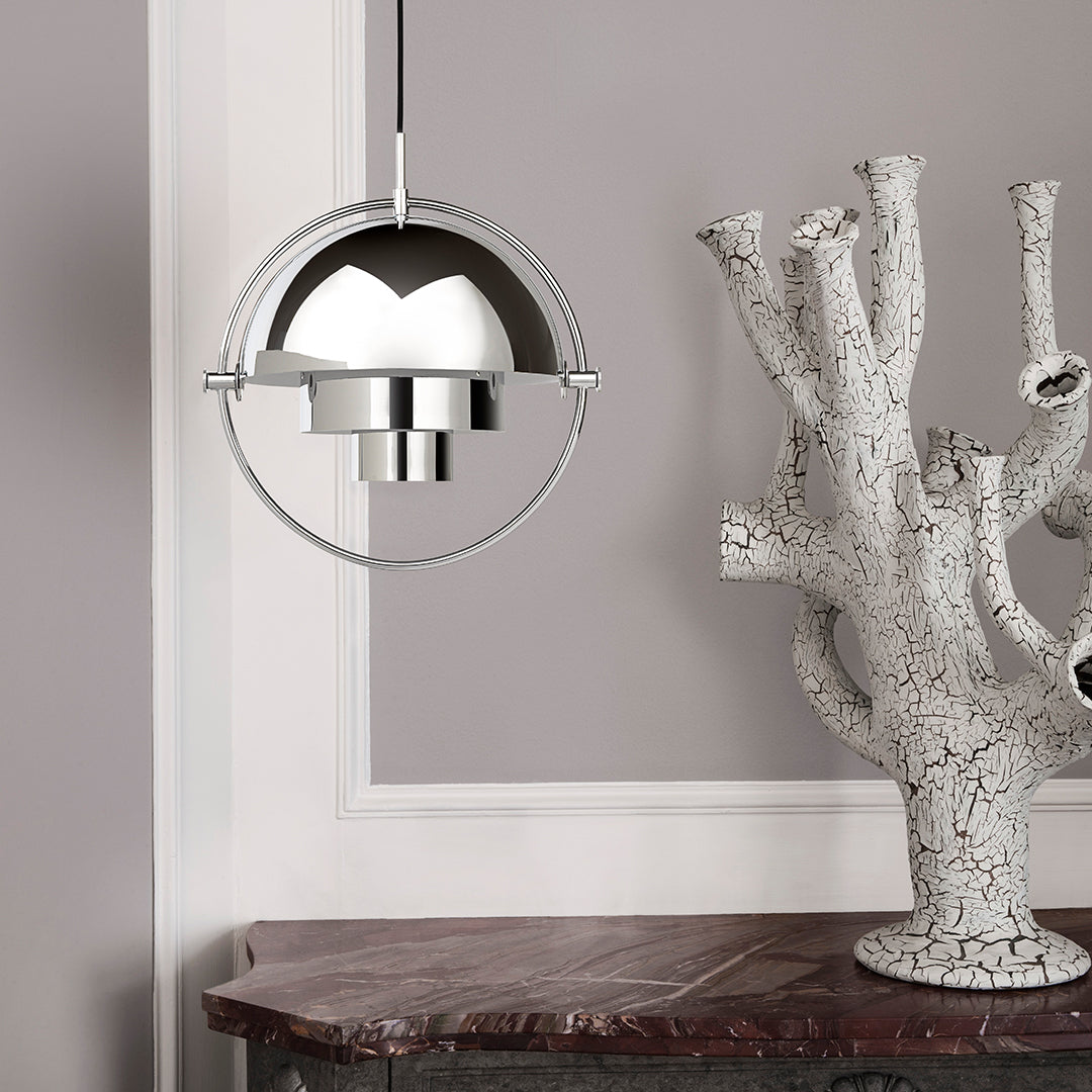Sleek metallic silver pendant light with a smooth spherical design against a soft gray wall and natural textures.