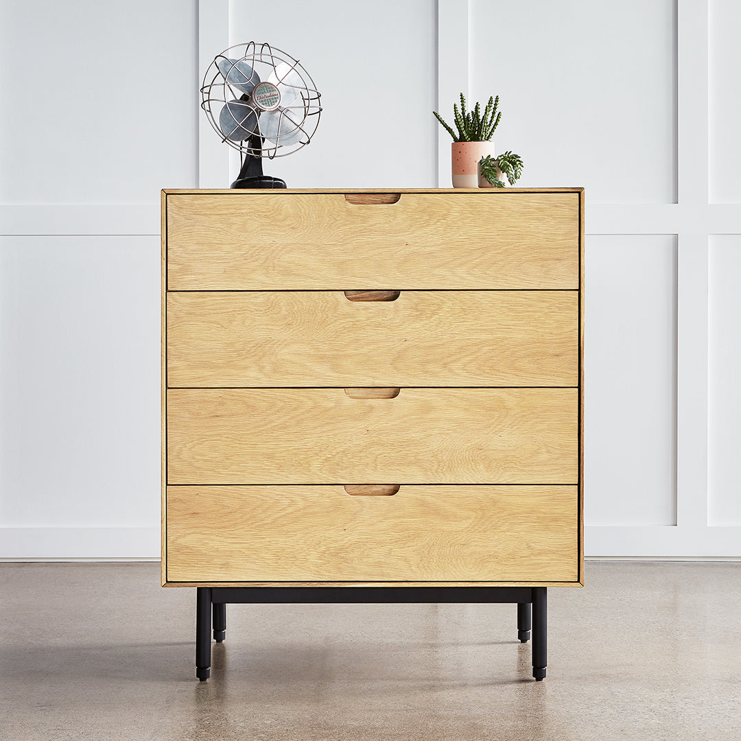 Light oak wood dresser with four drawers and black metal legs, set against a minimalist white background.