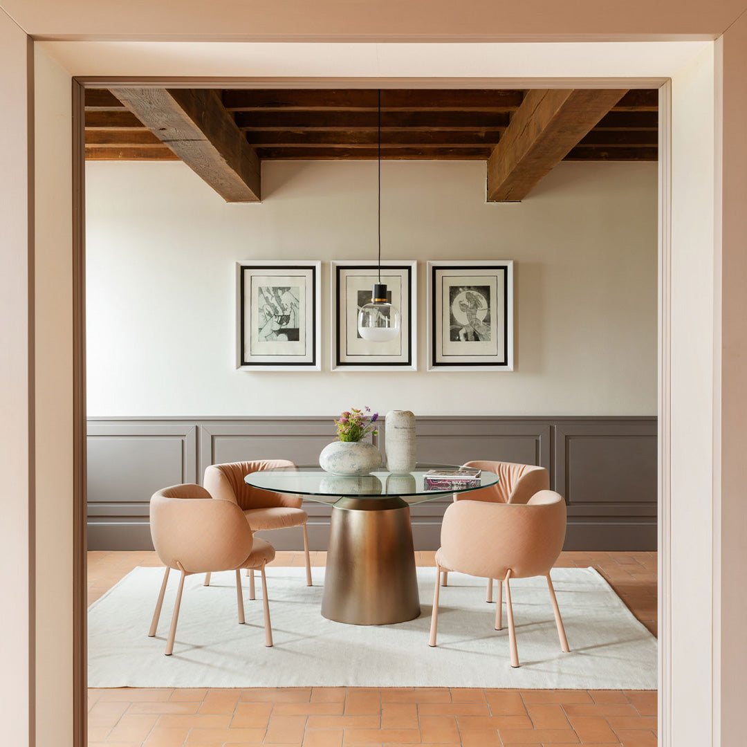 Elegant dining area featuring soft pink chairs, a round glass table, and textured neutral walls. Modern rustic vibe.