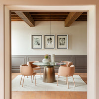 Elegant dining area featuring soft pink chairs, a round glass table, and textured neutral walls. Modern rustic vibe.
