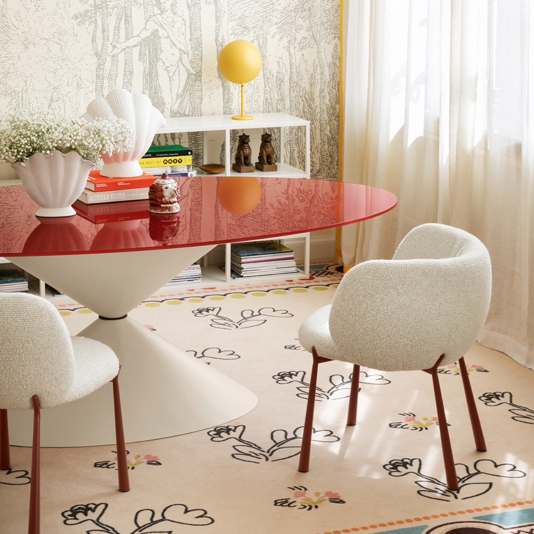 Red round table with white chairs against a pastel floral-patterned rug in a bright room.