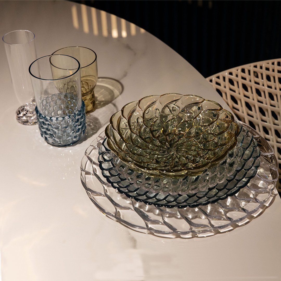 Glassware set featuring textured circular patterns in green, blue, and clear tones on a sleek white table.
