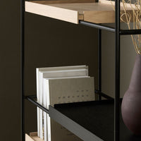 "Black metal shelf with natural wood accents, displaying stacked gray and white books, set against a dark background."