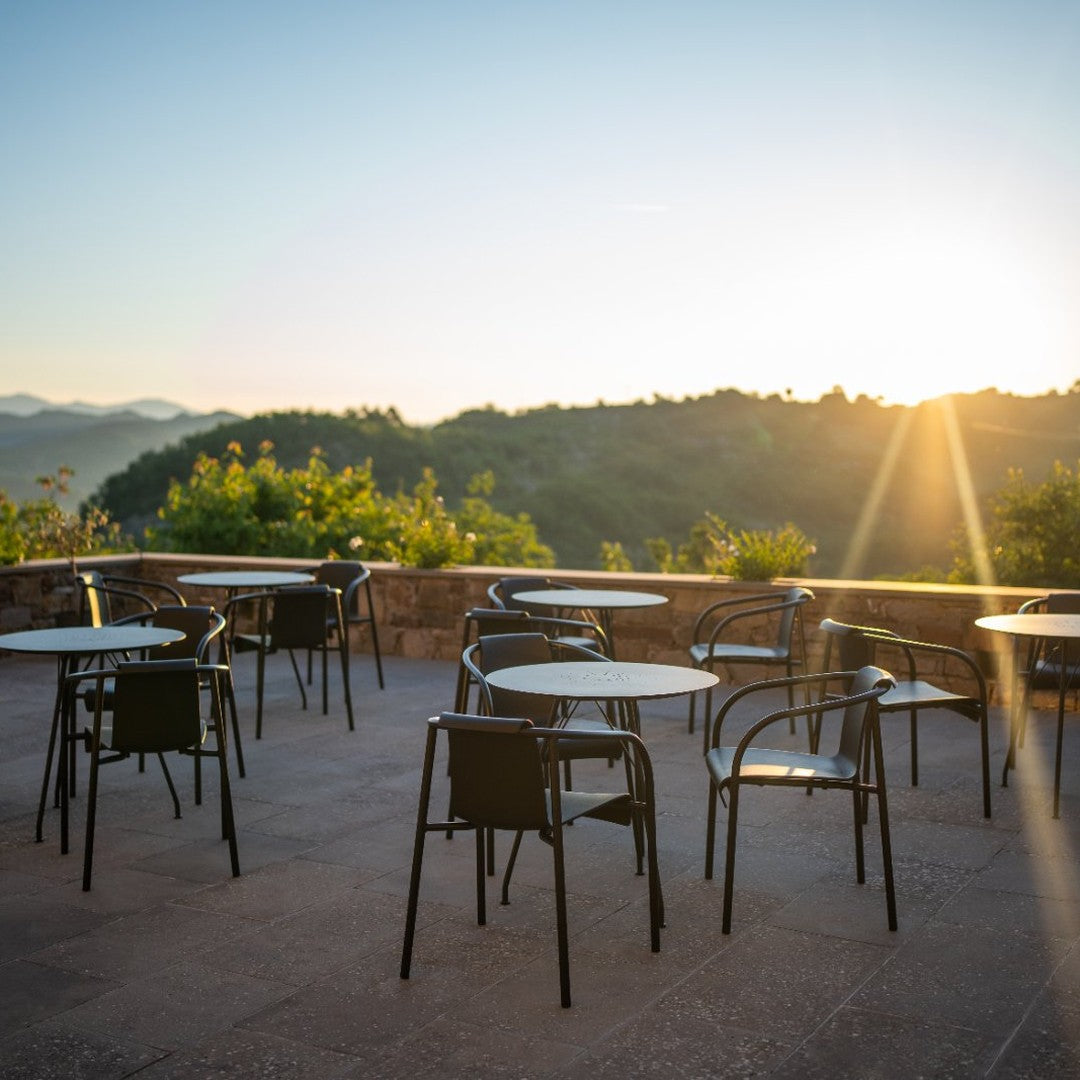 Black chairs and tables set against a sunlit landscape, featuring a natural stone terrace and soft morning light.